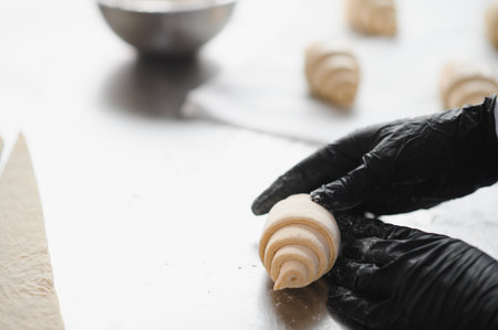 Baker wearing black gloves preparing croissants on a stainless steel table in a bakery kitchen