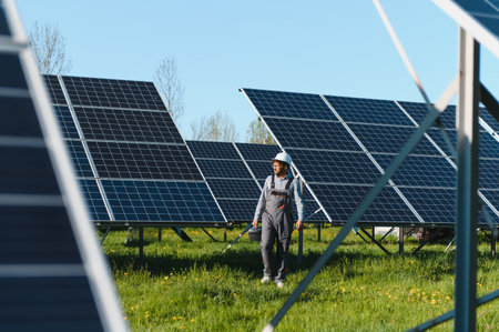 Middle eastern engineer walking in a solar panel farm, carrying tools and wearing overalls and...