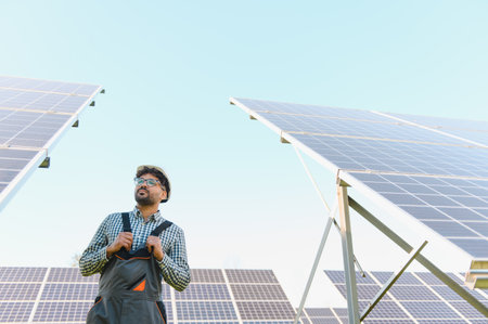Middle eastern engineer inspecting solar panels in a large photovoltaic plant under a clear blue sky