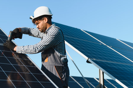 Professional technician using tools to install solar panels, highlighting renewable energy solutions and sustainable practices under a bright blue skyの写真素材