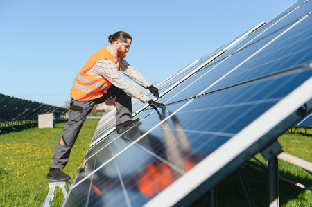 Male technician adjusting solar panels in a vast photovoltaic plant under the bright sun, ensuring...