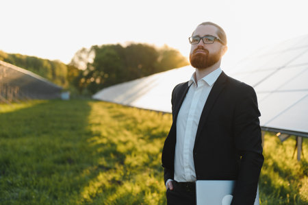 Businessman with laptop inspecting a solar panel farm at sunset, embracing sustainable energy...