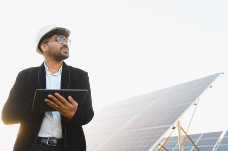 Young Indian engineer holding digital tablet inspecting solar panels in a photovoltaic power station