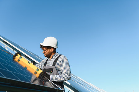 Middle eastern engineer uses a level tool while installing a solar panel on a clear day, promoting...