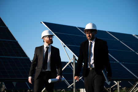 Two engineers walking through a solar panel farm, discussing project details and collaborating on...