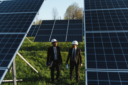 Two walking engineers through a vast solar panel farm, discussing innovative strategies for their...
