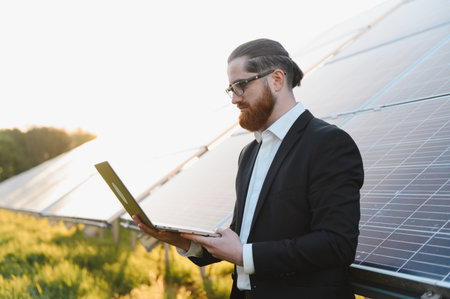 Businessman using laptop analyzing photovoltaic solar panels during sunset in a sustainable...