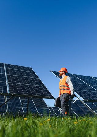 Male technician walking and carrying toolbox while inspecting solar panels in power plant under...