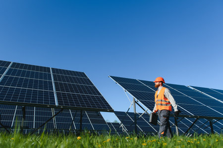 Electrical engineer carrying toolbox and walking near photovoltaic solar panels during maintenance...