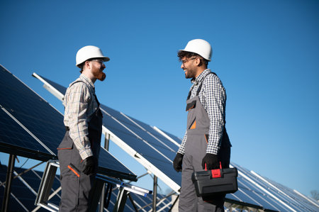 Two multi ethnic engineers talking and smiling during installation of photovoltaic panels in a solar...