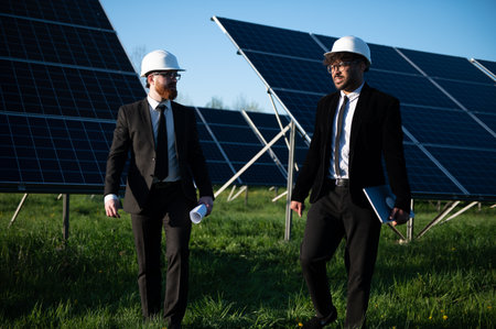 Two engineers walking through a solar panel farm, discussing project details and collaborating on...