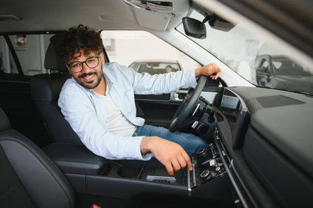Arab man adjusting car radio settings while sitting in driver's seat inside a new car at a...