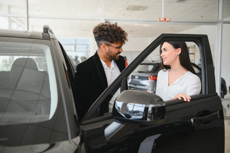Salesman engaging with a female customer, highlighting features of a new car in a modern dealership...