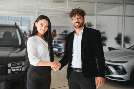 Salesman shaking hands with a female customer after closing a deal on a new car inside a modern car...