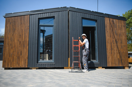 Construction worker moving a prefabricated modular house using a ladder, showing innovative building...