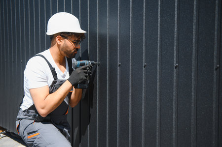 Skilled worker using cordless drill to install metal siding, focusing on precision and safety in...