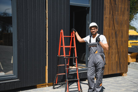 Construction worker in overalls and hardhat oversees the loading of a prefabricated modular house...