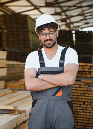 Portrait of a confident woodworker smiling with crossed arms, standing in a lumber warehouse,...