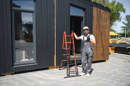 Construction worker in hardhat and overalls ensures the secure loading of a prefabricated modular...