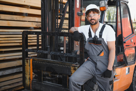 Portrait of a smiling warehouse worker leaning on a forklift, with stacks of lumber visible in the...