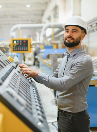 Industrial engineer wearing hardhat operating machinery in modern factory, controlling production...