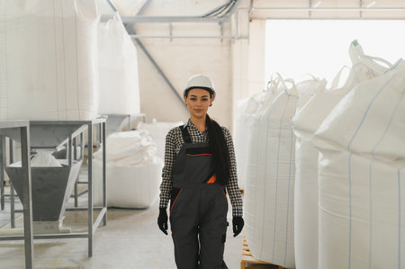 Young woman engineer wearing workwear and hardhat walking through a flour factory, inspecting...