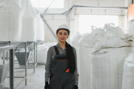 Confident female engineer wearing white hardhat and overalls standing in a factory.