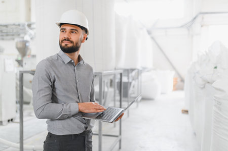 Food industry engineer wearing hardhat using laptop and inspecting production line in modern food...