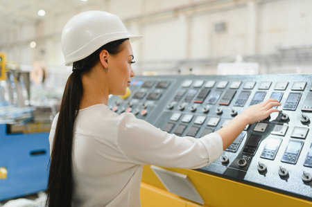Female industrial engineer wearing hardhat operating control panel of machinery in modern factory