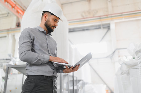 Industrial engineer wearing hardhat using laptop while inspecting operations in a food processing...