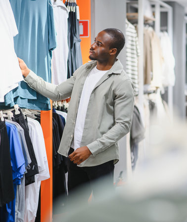 African american man exploring fashion choices in a mall, selecting stylish garments from a variety...