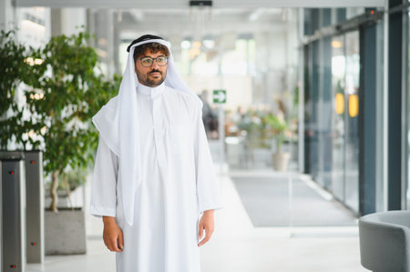 Confident arab businessman in traditional kandura walking through a modern office space, showcasing...