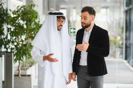 Two businessmen walking through a modern office building, discussing projects and plans while collaborating on strategies for successの写真素材