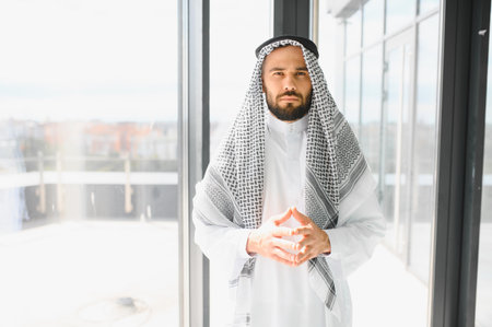 Portrait of a confident Arab businessman wearing traditional kandura and ghutra in a modern office, embodying cultural heritage and business acumenの写真素材