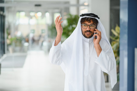 Successful entrepreneur gesturing and speaking on a smartphone while navigating a bright, modern office lobby, exuding confidence and professionalismの写真素材