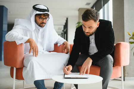 International operations manager signing a contract with a Saudi business partner wearing...