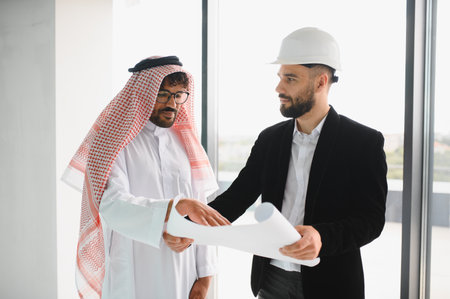 Arab investor and architect examining blueprints for a new business center project, highlighting...