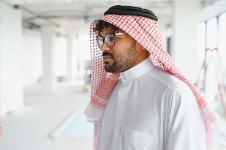 Arab architect wearing traditional clothing inspecting the construction site of a modern building, overseeing the project's progressの写真素材