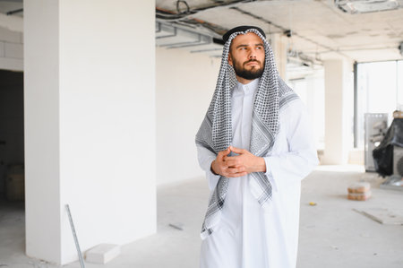 Arab businessman wearing traditional clothing standing in a new business center during construction, considering investment and developmentの写真素材
