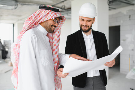 Arab investor and architect examining blueprints on a construction site, showcasing teamwork and...