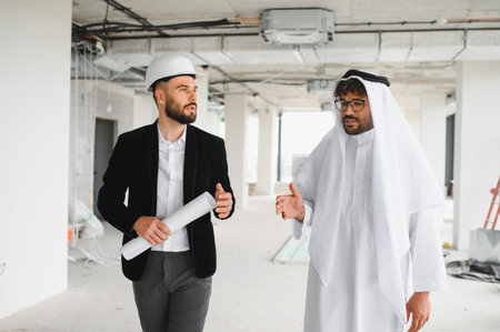 Architect holding blueprints discussing building plans with investor wearing traditional Arabic...