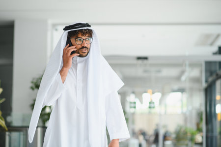 Arab businessman wearing a traditional kandura is using his smartphone in a modern building