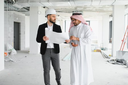 Architect wearing a hardhat, presenting a blueprint to an arab investor during a building...