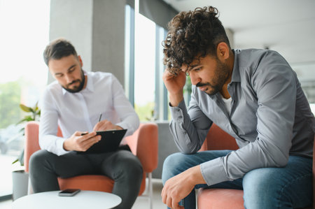 Upset arab man suffering from ptsd having a therapy session with psychologist taking notes on...