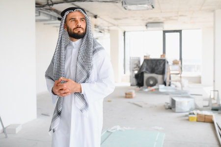 Arab businessman wearing traditional clothing evaluating progress at a construction site,...