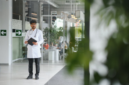 Young arab doctor standing in modern clinic hall holding a medical chart, representing healthcare, professionalism and expertiseの写真素材