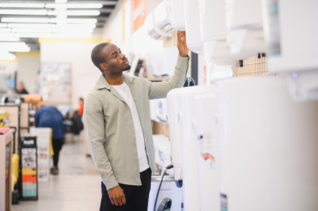 Young man selecting a new water heater in the appliance section of an electronics store, comparing...