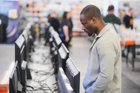 Customer comparing televisions in consumer electronics store, making purchasing decision for home...