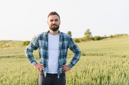 Confident agronomist standing with hands on hips, carefully inspecting a lush wheat field, preparing for the upcoming harvest seasonの写真素材