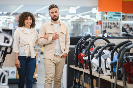 Young couple walking through an electronics store, discussing options and selecting the perfect vacuum cleaner for their homeの写真素材